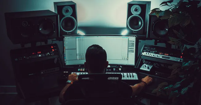 Professional music producer working in a modern home studio with audio equipment and digital audio workstation on screen.
