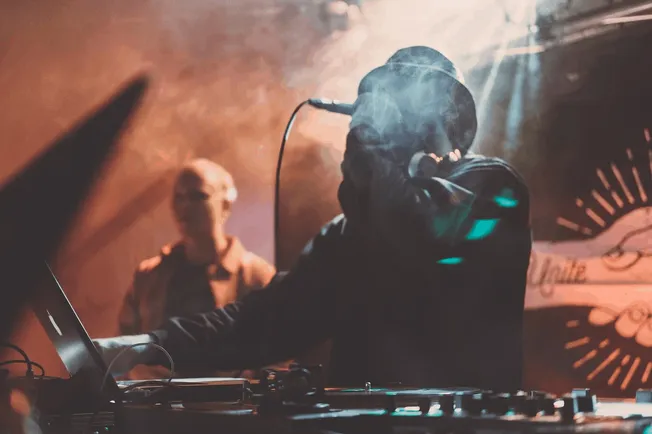 Dynamic DJ performing live with turntables and mixing console at a vibrant music event, illuminated by colorful stage lights