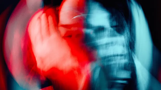 Blurred image of a person with red and blue lighting, expressing intense emotion, likely related to music or artistic perform