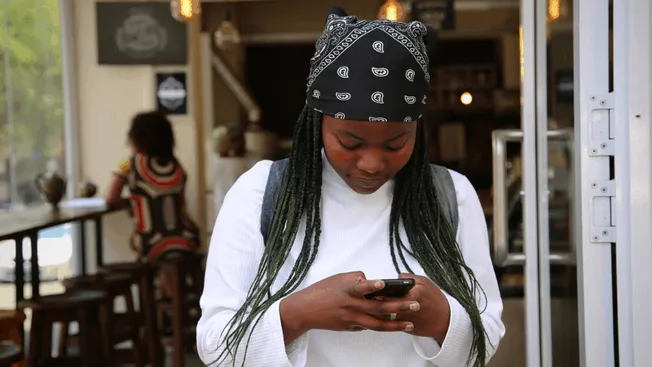 Music enthusiast using a smartphone in trendy cafe with a bandana and braided hair, embodying modern digital engagement in th