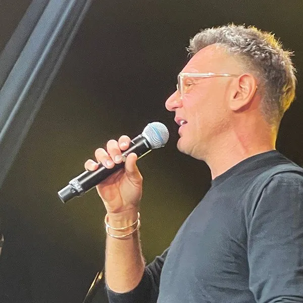 Microphone in hand, male speaker or singer performing at event, close-up profile image, on stage with dark background, popula