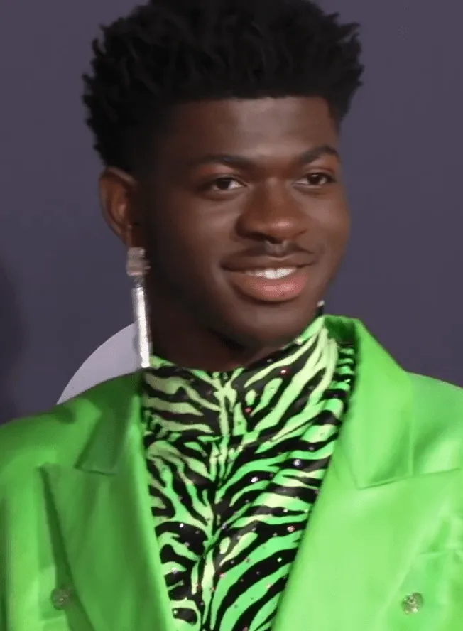 Black man wearing a vibrant green blazer and zebra-print shirt, stylishly dressed with an earring, smiling confidently at a f