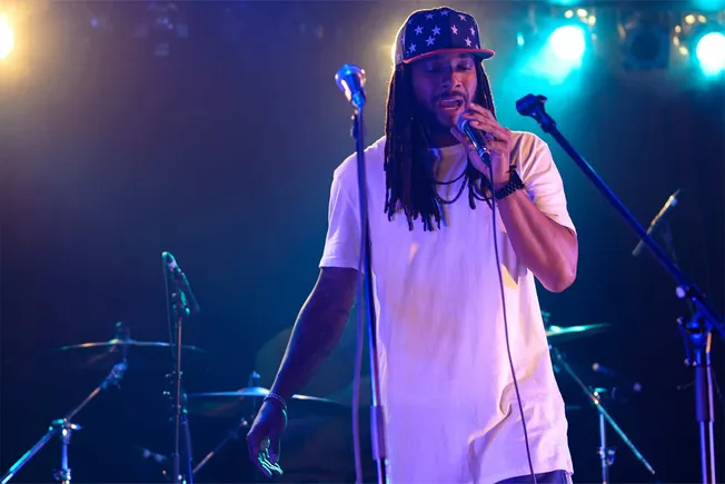 A dynamic performer singing into a microphone on stage during a live music concert with colorful stage lighting.