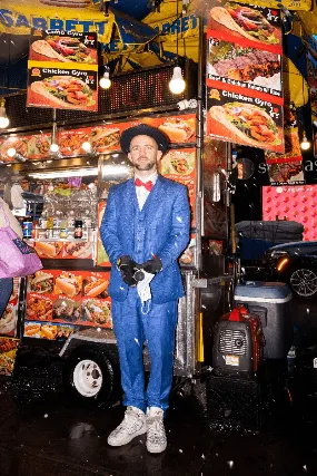Vibrant street food vendor standing amidst colorful food stall with chicken dishes, illuminated by warm lighting, capturing l