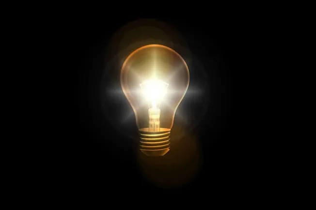 Illuminated incandescent light bulb glowing in darkness symbolizing ideas and innovation.
