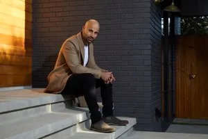 Man sitting on stairs outside modern building, urban environment, casual attire, relaxed pose.