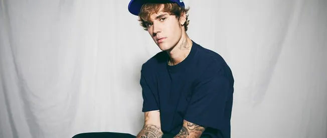 Young male musician with tattoos wearing a blue shirt and cap, studio portrait.