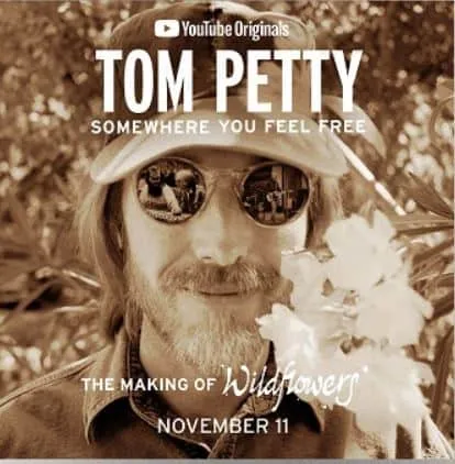 Serene portrait of Tom Petty wearing sunglasses with trees and foliage in the background, promoting his song "Somewhere You F