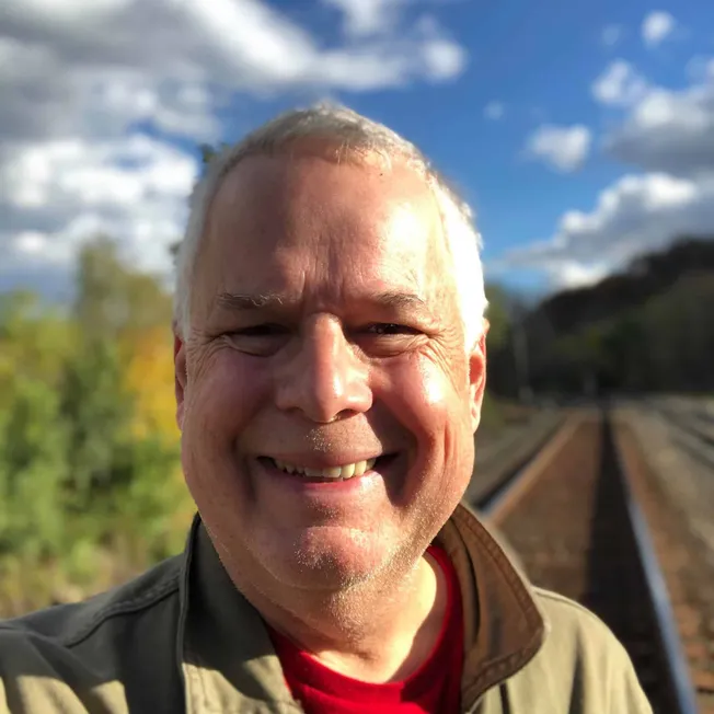 Smiling man outdoors near railway tracks on a sunny day with blue sky and clouds, representing music industry insights, digit