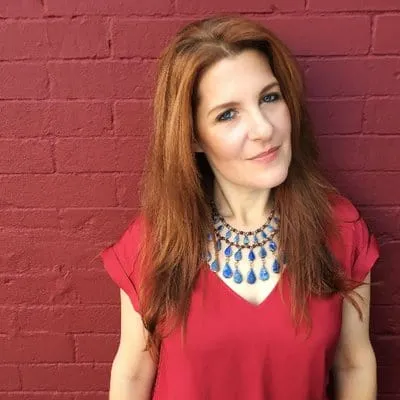 Vibrant woman with red hair in front of a red brick wall, wearing a red blouse andStatement necklace, showcasing modern fashi