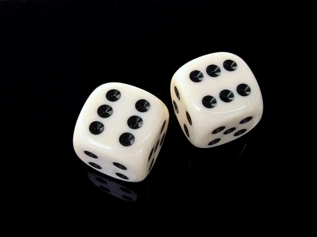 White dice with black pips on a glossy black surface, illustrating chance and probability concepts.