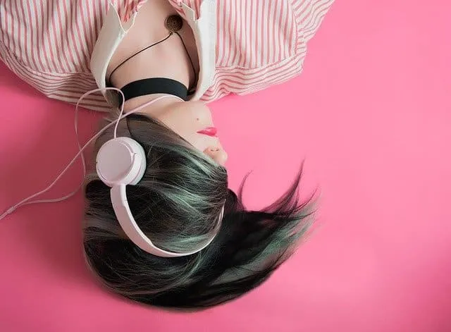 Girl listening to music with headphones lying on pink background, relaxed and enjoying her favorite tunes, digital music, hea