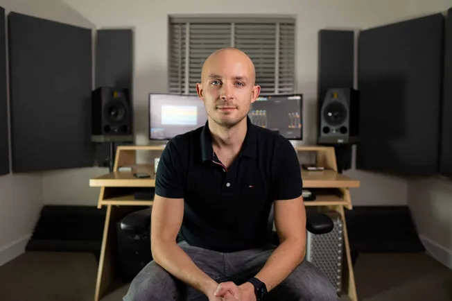 Bald man in music studio with professional sound equipment, mixing consoles, studio monitors, and acoustic panels, creating a