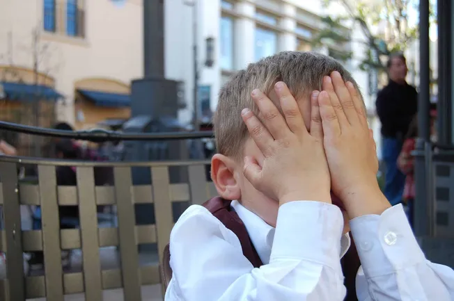 Frustrated young boy covering his face with hands sitting outdoors, illustrating emotional distress or disappointment at a pu
