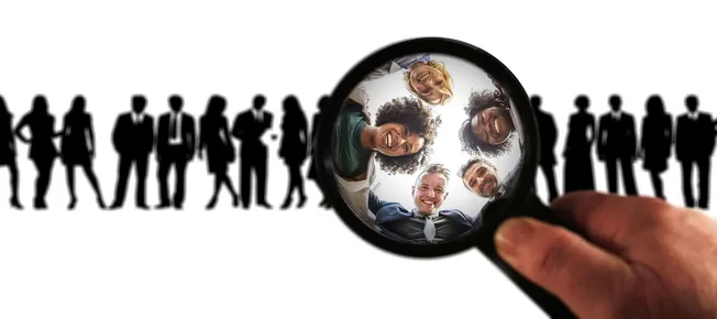 Diverse group of professionals smiling, viewed through a magnifying glass focusing on the faces, representing talent search a