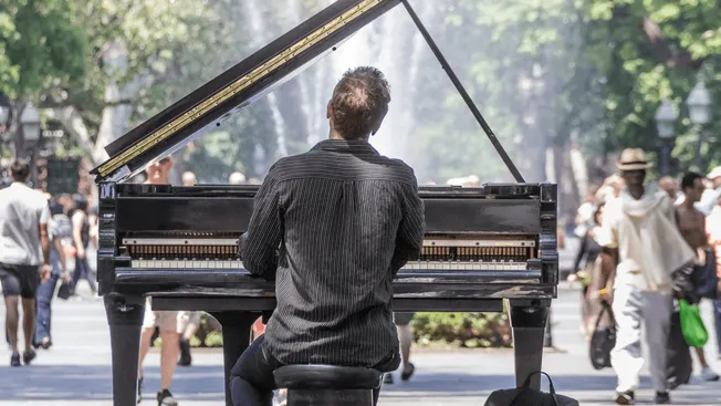 A pianist performing outdoors in a busy city park, capturing the vibrant live music scene and street culture.