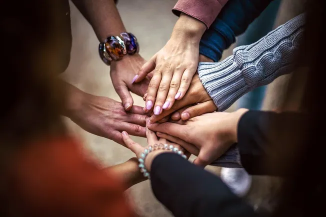 Hands joined together in a circle, symbolizing unity, teamwork, and collaboration in a diverse group, representing community