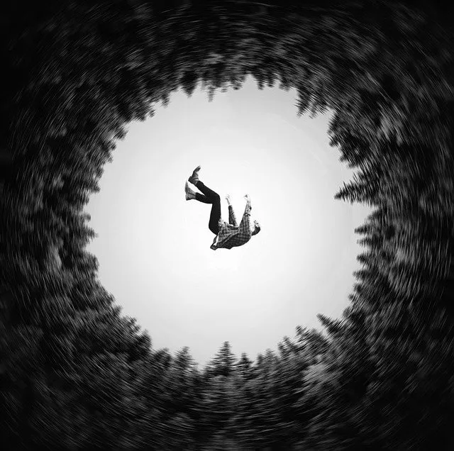 A person falling through a swirling black and white vortex surrounded by trees at the edge of a forest.