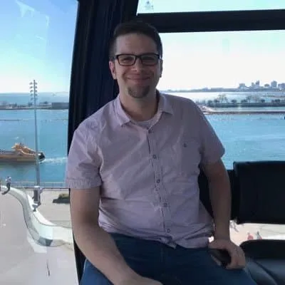 Bright young man sitting by waterfront window, enjoying a peaceful moment, featuring a modern indoor setting with blue skies