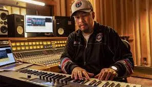 Studio music producer operating mixing console with audio equipment and keyboard, in professional recording studio.