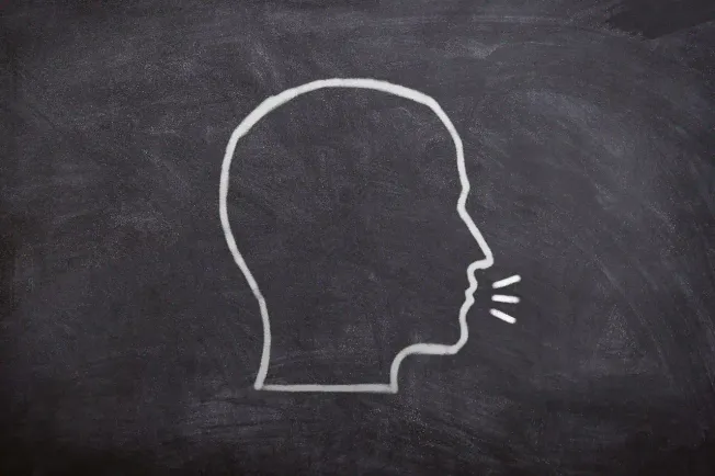 Silhouette of a person's head drawn with white chalk on a blackboard, with lines indicating speaking or communication.