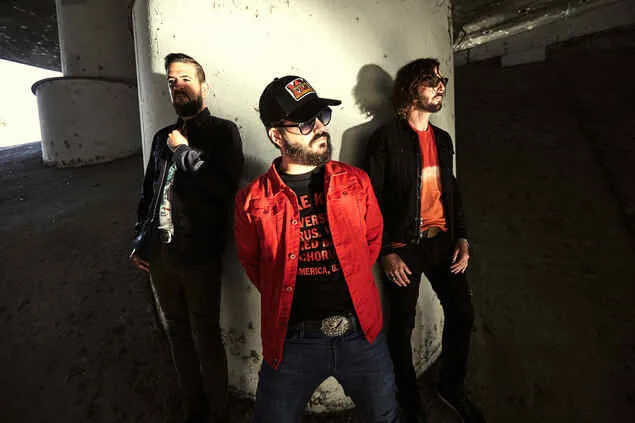 Three men in trendy casual clothing standing under a bridge, showcasing modern music culture and urban aesthetics, representi