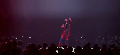 A performer on stage during a concert with dramatic lighting, engaging the audience.