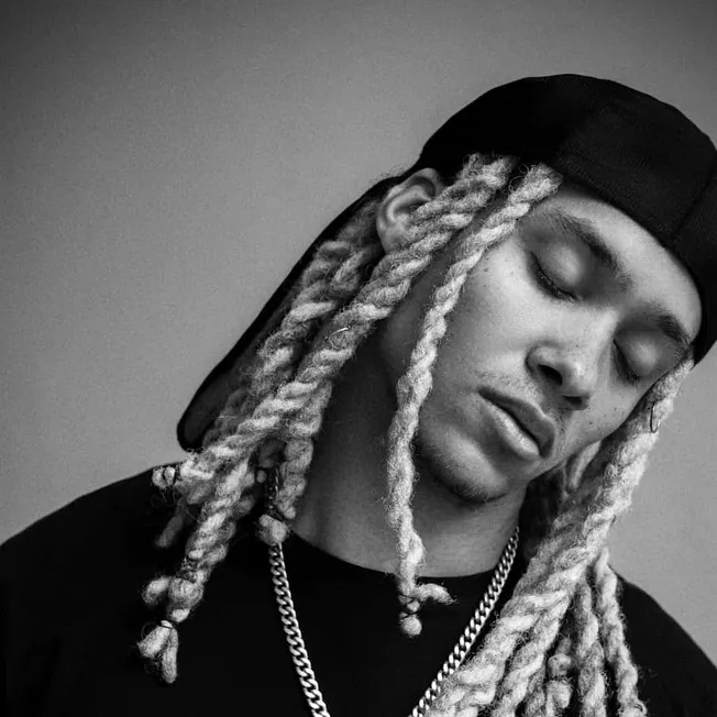 Vape artist with long blonde dreadlocks, wearing a backwards hat and chain, black and white portrait, streetwear style, repre