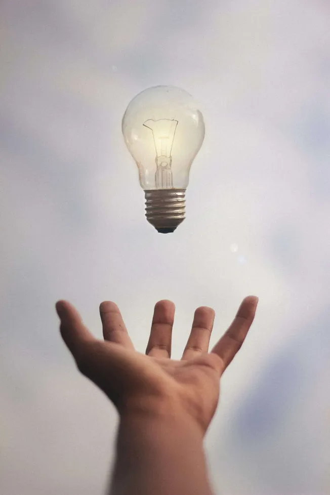Innovative thinking concept with hand tossing a lightbulb into the sky symbolizing ideas and creativity.