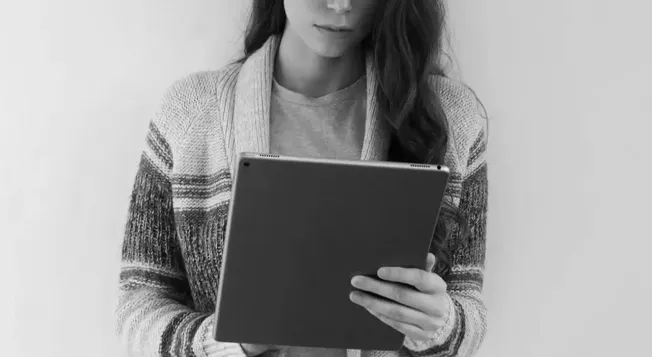 Woman using tablet device, digital media consumption, modern technology, casual attire, black and white photo.