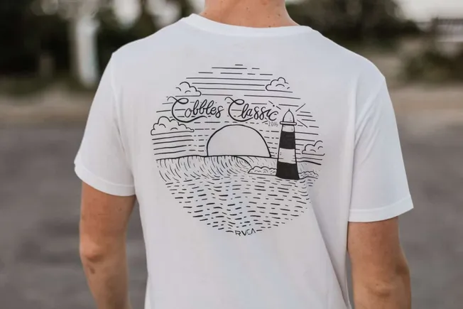 Clouds and sun illustration on a white t-shirt featuring a lighthouse and ocean scene, popular for casual wear and surf-inspi