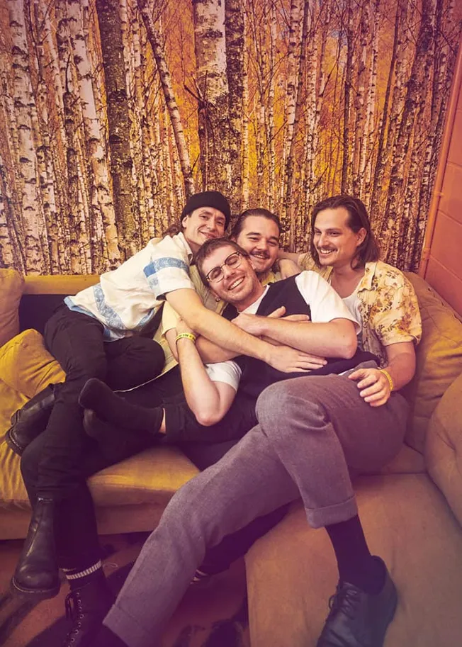 Happy group of friends sitting on a cozy yellow couch in front of a autumn forest-themed wall backdrop, enjoying fun moments