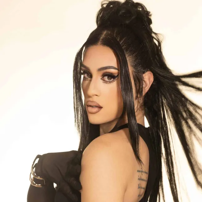 Vibrant portrait of a woman with striking makeup, long black hair, and tattooed shoulder, showcasing contemporary fashion and