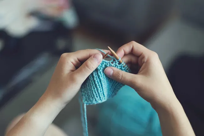 A person knitting with blue yarn and wooden needles, demonstrating craft and DIY skills, close-up of hands, handmade knitting