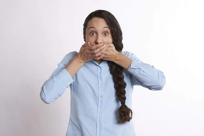 Sensitive woman with hands covering her mouth, expressing shock or surprise.