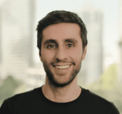 Professional male with dark hair and beard, smiling in an urban cityscape background, representing music industry news, digit