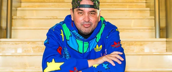 Stylish man in colorful hoodie with streetwear accessories sitting on wooden stairs, representing music culture, urban fashio