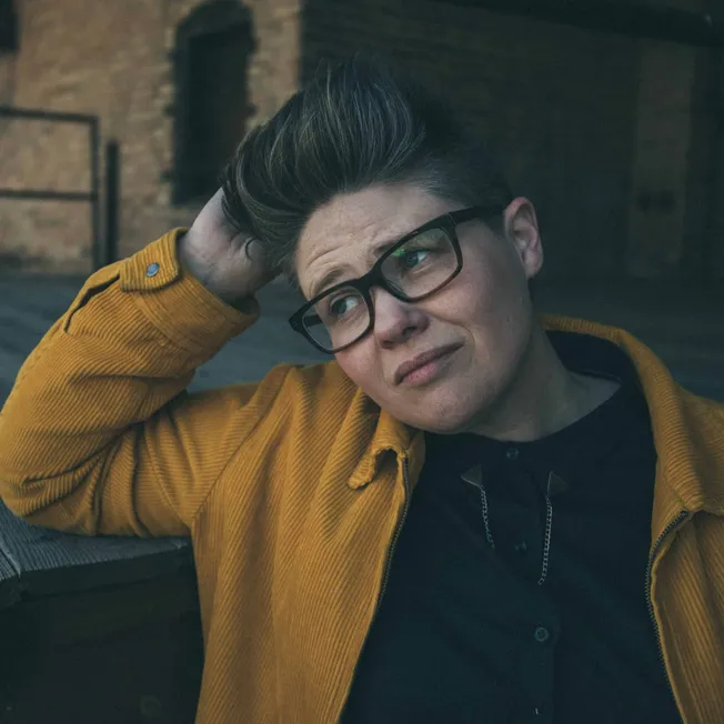 Innovative woman with glasses in a yellow jacket sitting outdoors, showcasing contemporary style and urban lifestyle for musi