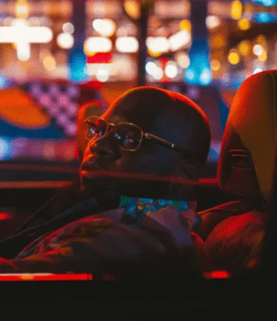 Person relaxing in a convertible car at night with city lights in background, illustrating lifestyle and nightlife themes fro