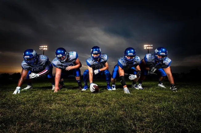 Team of American football players in blue uniforms preparing for game on a grassy field under evening sky.