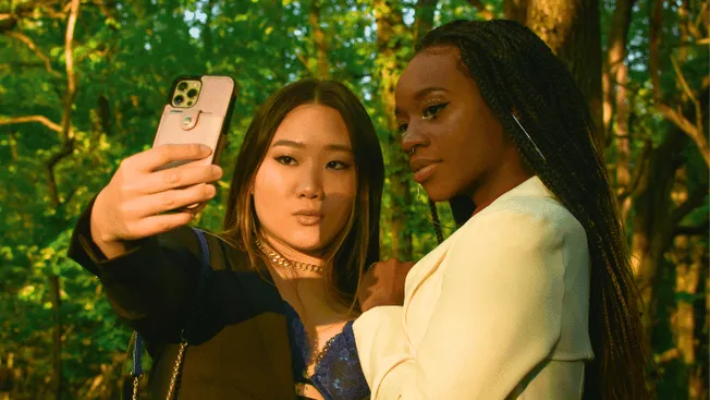 Selfie of two diverse women taking an outdoor photo in a lush forest setting, showcasing friendship, diversity, and nature ph
