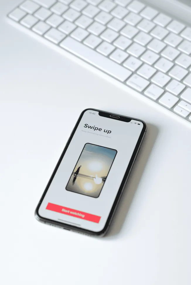Screenshot of a smartphone displaying a swipe-up video feature on a white desk with a keyboard in the background, illustratin