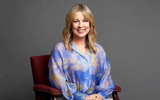 Bright smiling woman sitting on a red chair, wearing a colorful blue and yellow blouse with a gray background. Editorial port