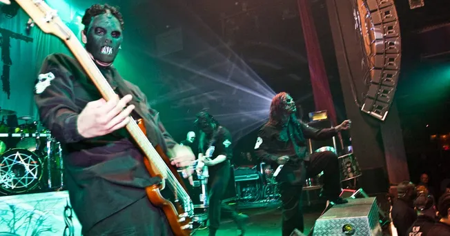 Dark masked guitarist performing live at a concert with dramatic lighting and stage effects, capturing the energy of a heavy