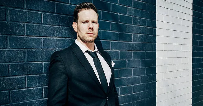 Professional businessman in a tailored suit standing against a modern brick wall, representing insights on the music industry
