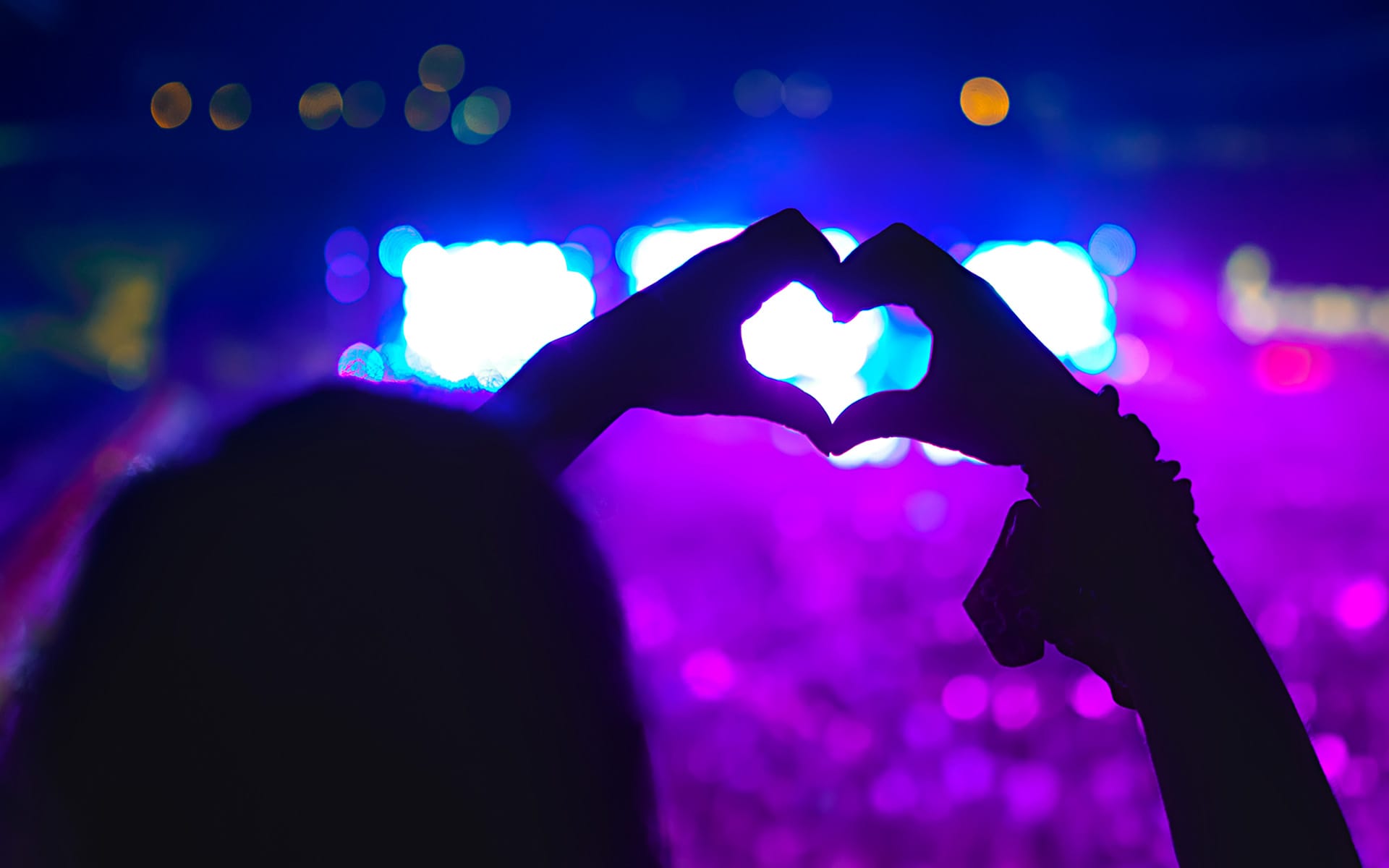 A person making the shape of a heart with their two hands at a Taylor Swift concert.
