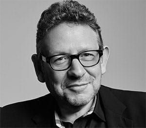 A professional black-and-white portrait of a man wearing glasses, dressed in a suit, smiling confidently. Suitable for articles on music industry insights, digital marketing, and media innovation.