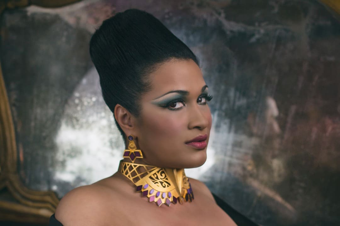 Elegant woman with dramatic makeup and statement jewelry, inspired by Afrocentric fashion, posing in a luxurious setting.