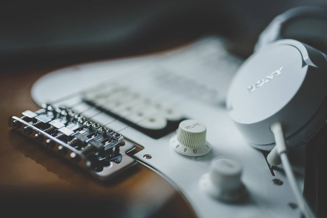Electric guitar with studio headphones, music production equipment, close-up shot of guitar controls and sound gear, professional music recording setup for artists and musicians, Hypebot music industry news and technology.