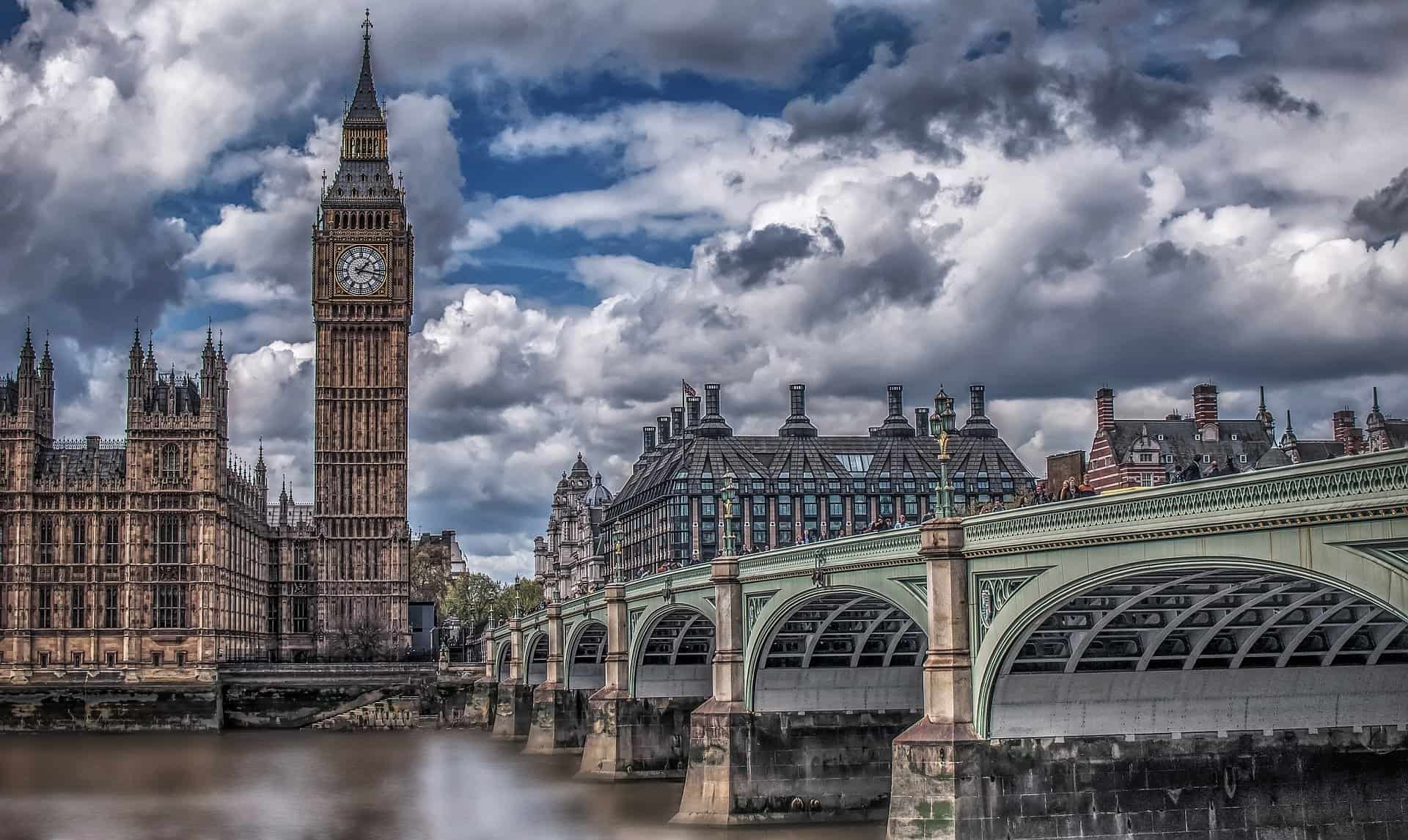 London Big Ben clock tower and Westminster Bridge over the Thames River under dramatic cloudy sky, iconic UK landmarks, historic architecture, travel destination, cityscape photography.